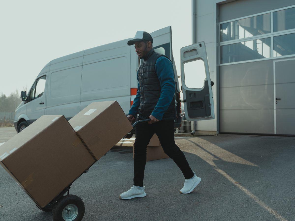 A mover wheeling a loaded trolley of boxes to a waiting van